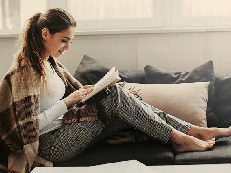 Frau entspannt mit einem Buch auf dem Sofa