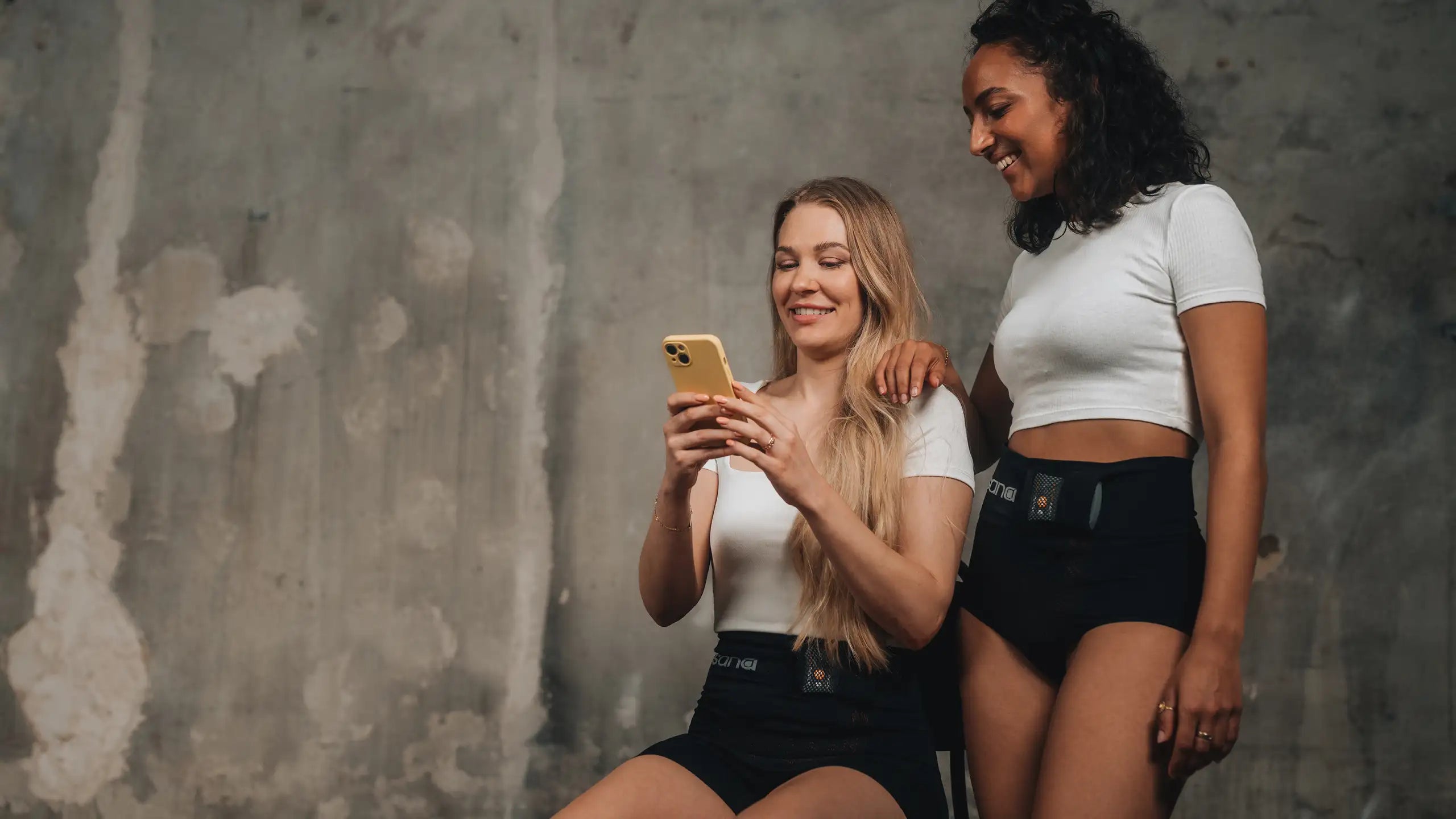 Zwei Frauen haben die sana-Produkte an und schauen auf die heat app